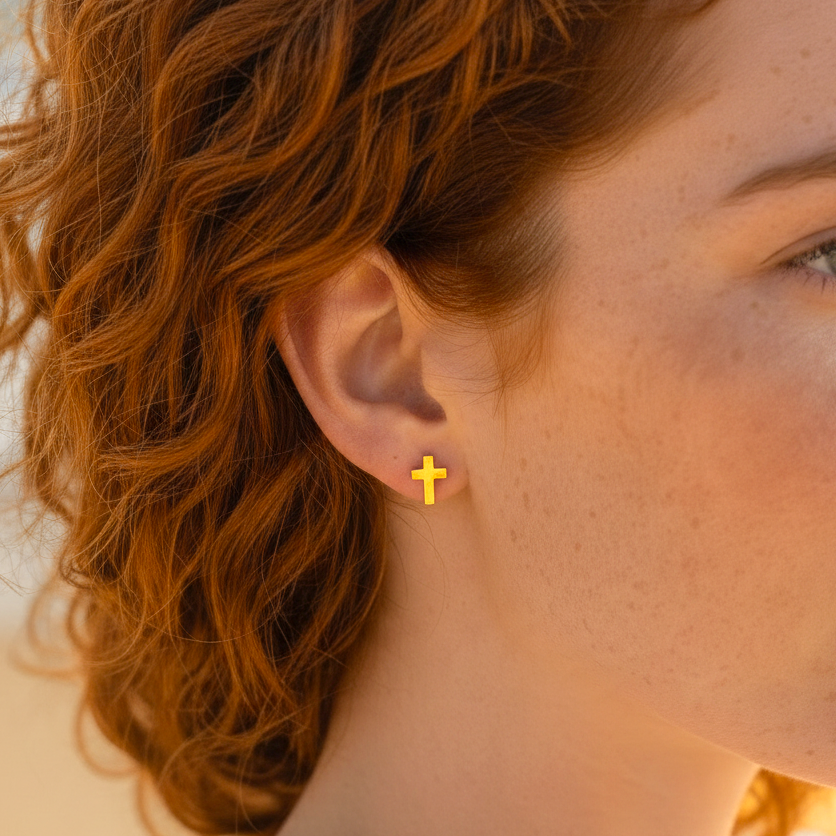 Mellow Monkey minimalist 18k gold cross stud earrings worn by a woman with red hair on a sunny beach