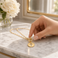 Mellow Monkey 18k gold paperclip chain necklace featuring a round cross pendant and a chic toggle clasp on marble
