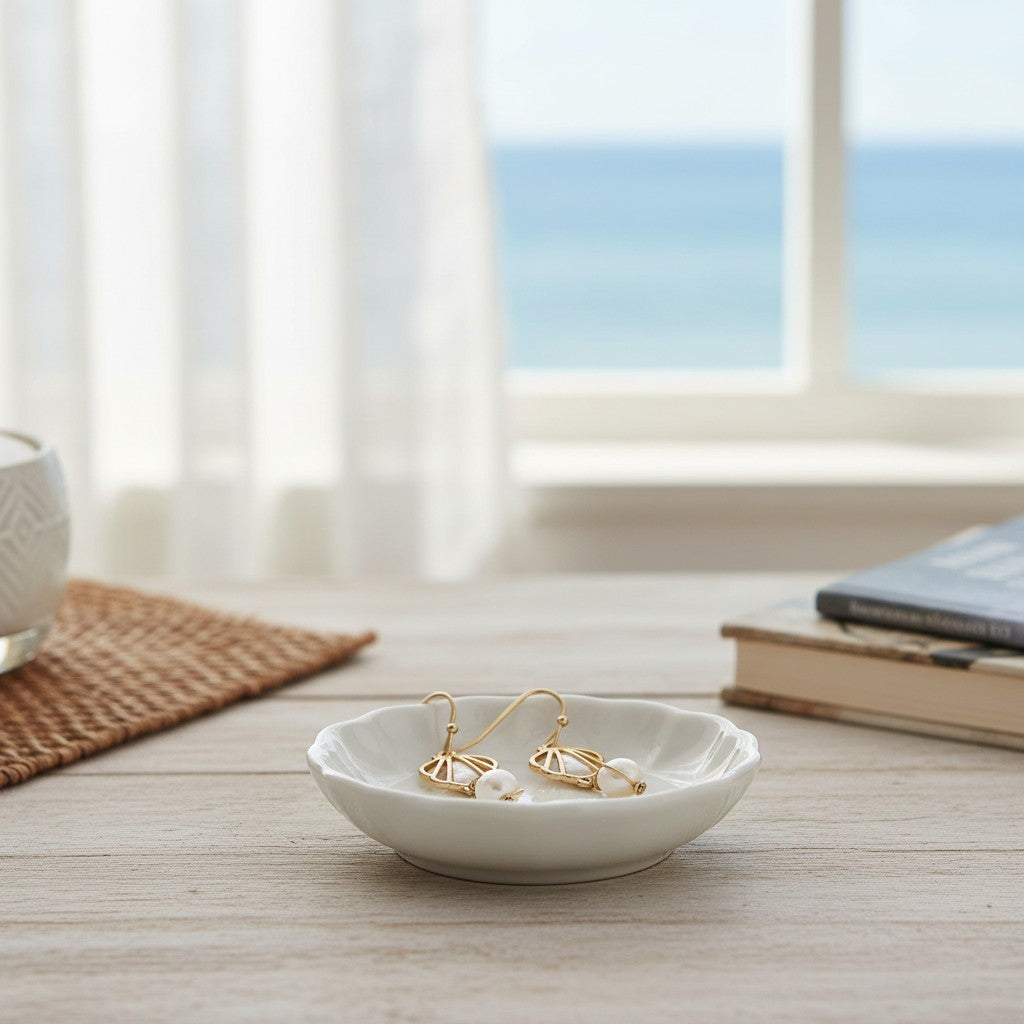Mellow Monkey gold open scallop earrings with white pearls displayed in a small white dish by a beach view window.