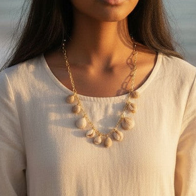 Mellow Monkey gold paper clip chain necklace with horn and clam shells, worn by a woman on a beach.