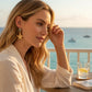 Mellow Monkey gold starfish earrings with aqua crystals worn by a woman overlooking the ocean at sunset.