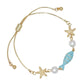 Mellow Monkey gold-tone adjustable bracelet featuring starfish, white pearls, and an aqua blue enamel fish charm.