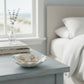Mellow Monkey gold starfish and pearl dangle earrings resting in a white shell dish on a coastal bedroom nightstand.