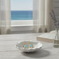 Mellow Monkey gold turtle earrings with blue marble enamel on a white shell dish by a coastal window.
