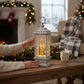 Mellow Monkey white lantern with a golden angel figurine and swirling glitter, set on a rustic wooden table.