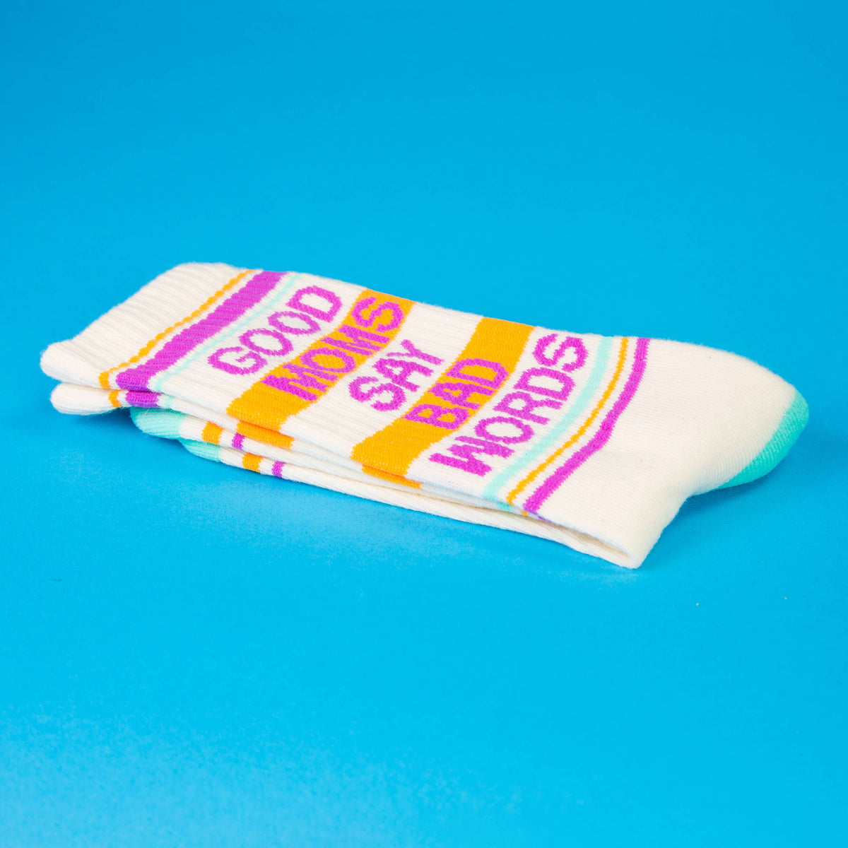 Mellow Monkey crew socks in white with Good Moms Say Bad Words text in colorful stripes on a bright blue background.