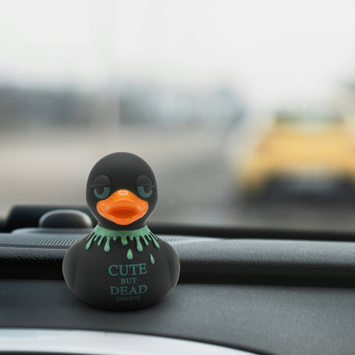Mellow Monkey gothic rubber duck with neon green blood drips and Cute But Dead Inside text on a car dashboard