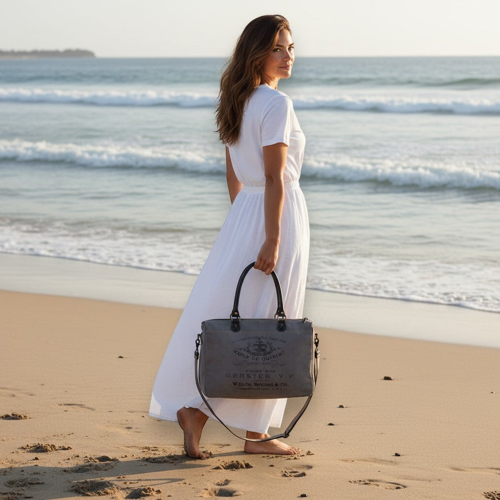 Mellow Monkey Grays Inlaid messenger bag in grey cotton and leather held by a woman in a white dress on the beach.