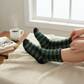 Mellow Monkey green and black plaid sleeper crew socks on a person lounging with a book and coffee