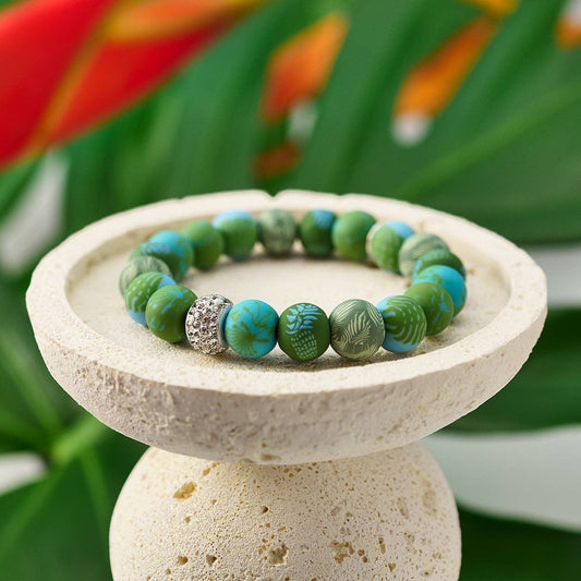 Mellow Monkey tropical green polymer clay bead stretch bracelet with a sparkling crystal center bead on a stone stand.