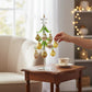 Mellow Monkey 10-inch glass Christmas tree with green branches and gold and white ornaments on a wooden side table
