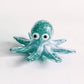 Mellow Monkey green glass octopus figurine with white and black eyes, detailed swirling patterns on a white background.