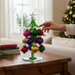Mellow Monkey 6-inch green glass Christmas tree with colorful swirled ornaments on a wooden table