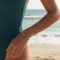 Mellow Monkey stretch seed bead bracelet in green and ivory with 18k gold plated accents worn on a beach.