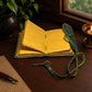 Mellow Monkey green embossed leather journal with antique key closure and yellow deckle edge paper on a wooden desk.