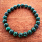 Mellow Monkey green malachite synthetic stone bead bracelet with 8mm beads on a wooden surface.