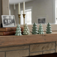 Mellow Monkey set of six small green stoneware Christmas tree figurines displayed on a rustic wooden fireplace mantel