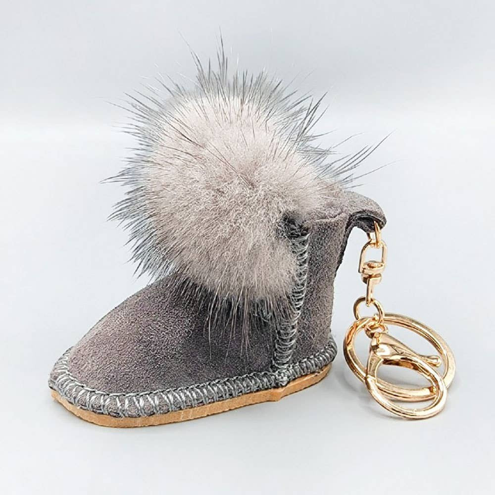 Mellow Monkey grey suede-like boot keychain with fluffy grey pom-pom accent and gold hardware.