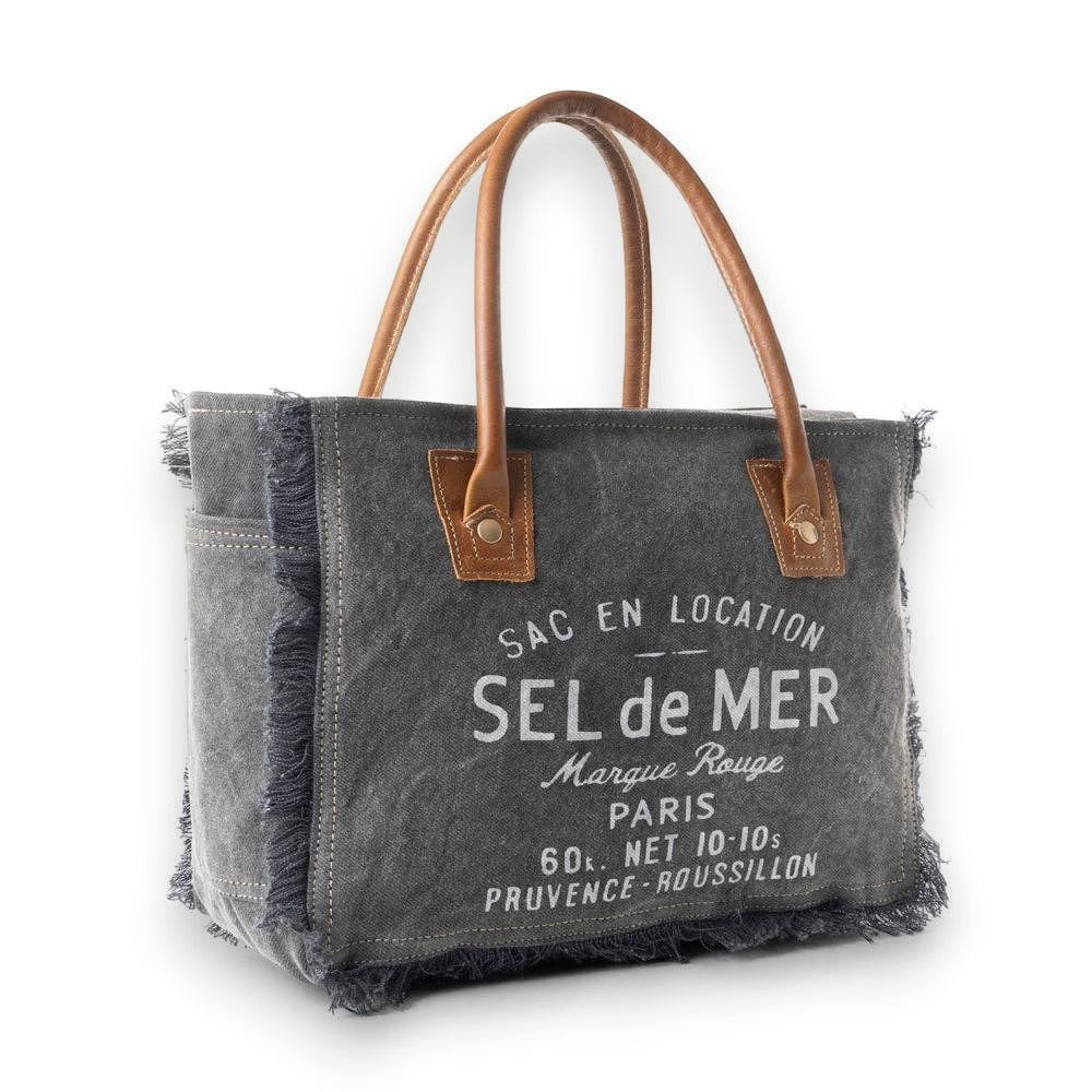 Mellow Monkey grey canvas crossbody bag with brown leather handles and frayed edges featuring vintage French typography