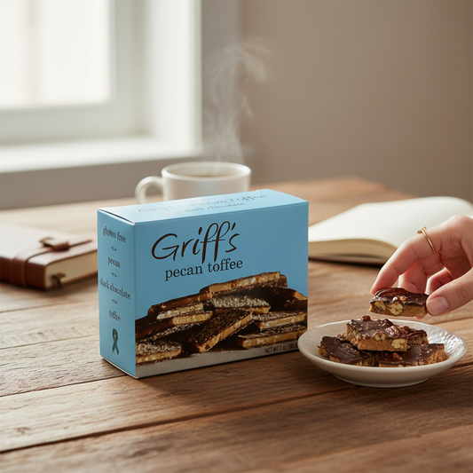 Mellow Monkey Griff's Pecan Toffee box with a hand serving dark chocolate pecan toffee pieces on a wooden table.