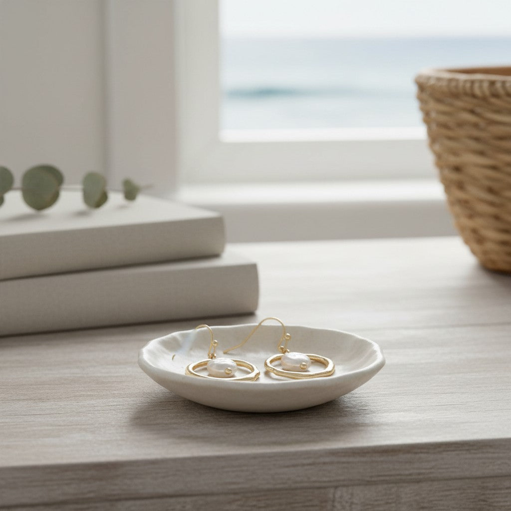 Mellow Monkey hammered gold earrings with white pearl drops resting on a small ceramic dish by a coastal window.
