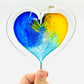 Mellow Monkey 5-inch hand-blown glass heart ornament featuring vibrant blue and yellow swirls on a clear glass base.