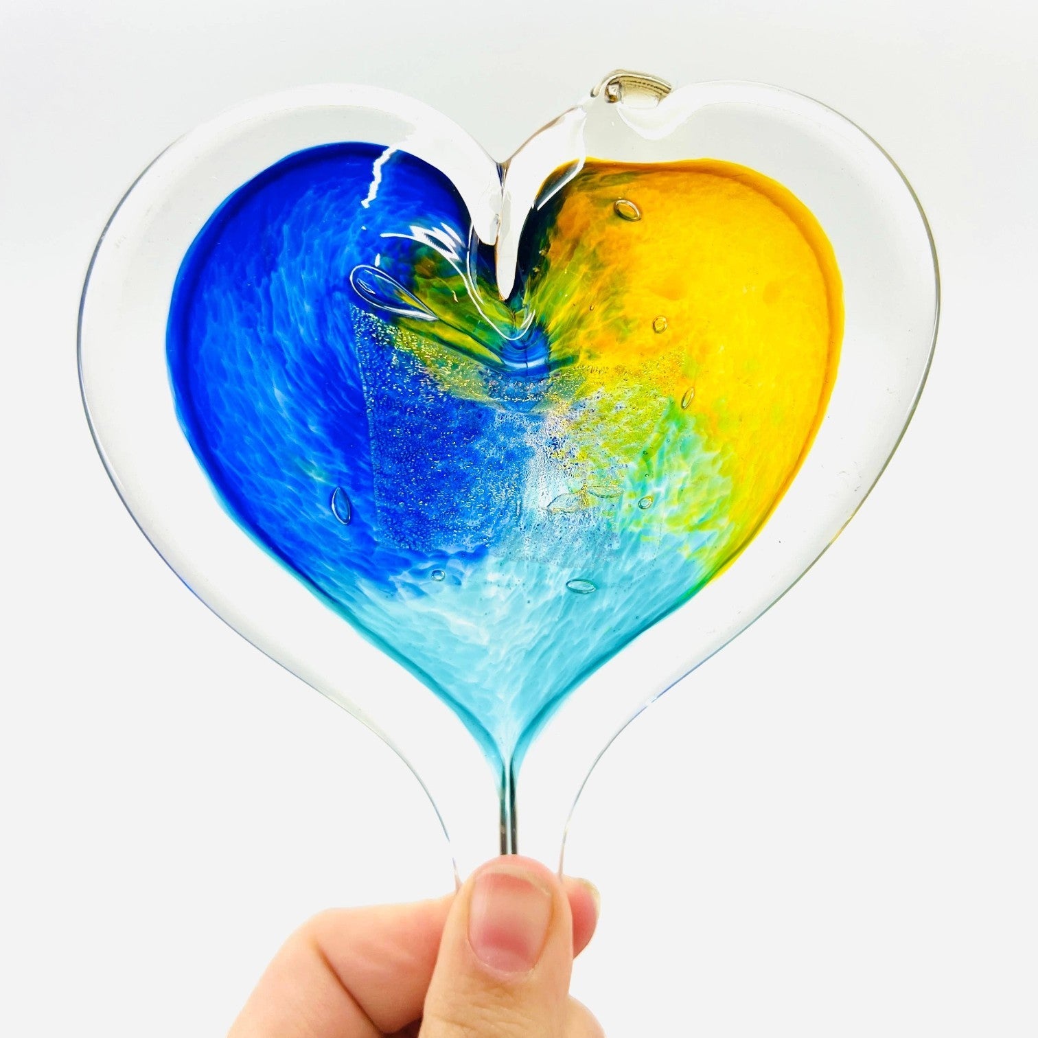 Mellow Monkey 5-inch hand-blown glass heart ornament featuring vibrant blue and yellow swirls on a clear glass base.