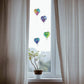 Mellow Monkey hand-blown glass heart ornaments in various colors hanging in a bright window