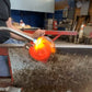 Mellow Monkey artisan hand-blown red glass heart ornament being shaped with a torch in a glassblowing studio