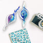 Mellow Monkey hand-blown glass spiral ornaments in blue and purple, featuring swirling light-catching designs.