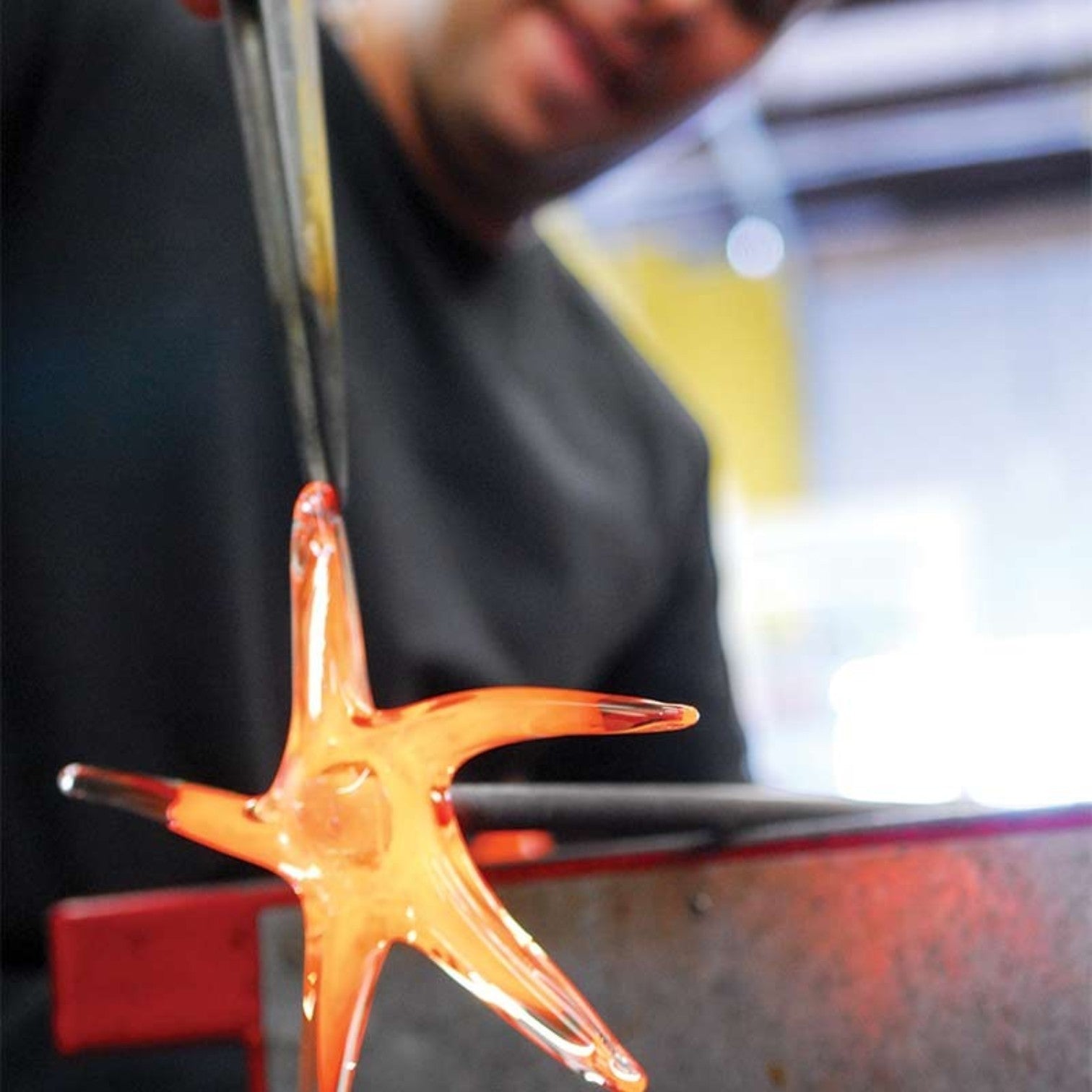 Mellow Monkey hand-blown glass star being shaped by a glassblower with metal tongs in a studio setting