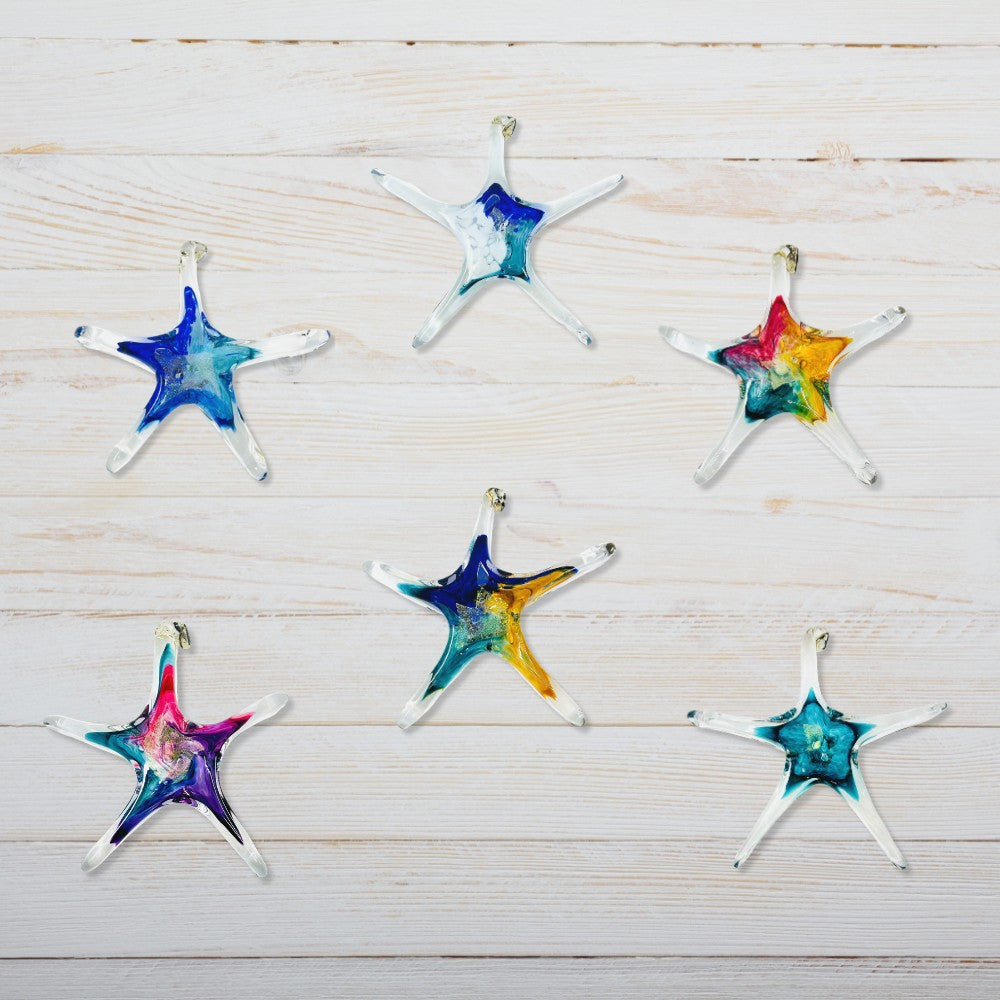 Mellow Monkey hand-blown glass star ornaments in various vibrant colors on a white wooden background