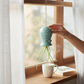 Mellow Monkey light blue hanging ceramic air plant holder with a live Tillandsia plant held by a hand near a window