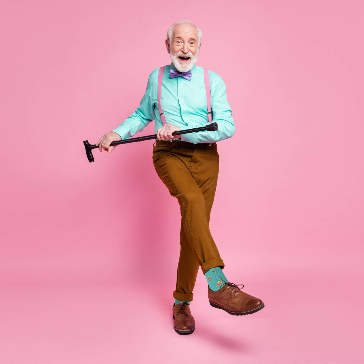 Mellow Monkey Happy Retirement socks worn by a joyful elderly man in a teal shirt, pink suspenders, and brown pants.