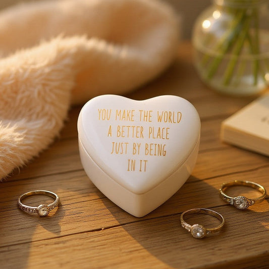 Mellow Monkey white ceramic heart-shaped trinket box with gold-foiled inscription on a wooden surface with rings.