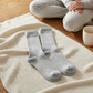 Mellow Monkey heather gray ribbed crew socks resting on a soft cream knit blanket next to a person in lounge wear.