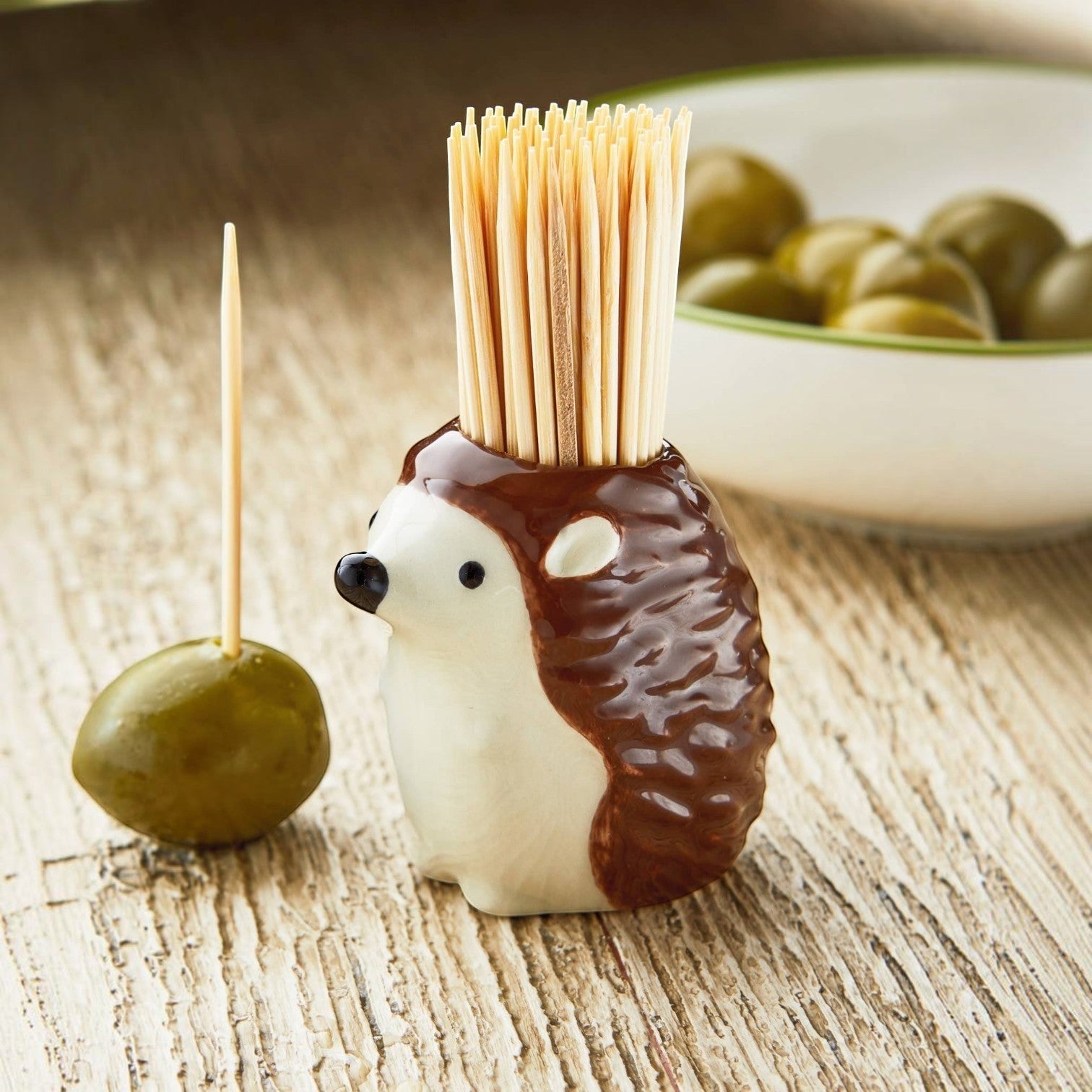 Mellow Monkey brown ceramic hedgehog toothpick holder with bamboo toothpicks on a wooden table with olives