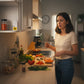 Mellow Monkey hidden cat meow prank device placed on a kitchen shelf, confusing a woman cooking dinner.