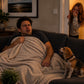 Mellow Monkey Hidden Rooster prank device causing confusion for a man on a couch while a woman laughs in the doorway.