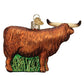 Mellow Monkey Highland Cow blown glass ornament with long horns and shaggy brown coat, on green grass base.