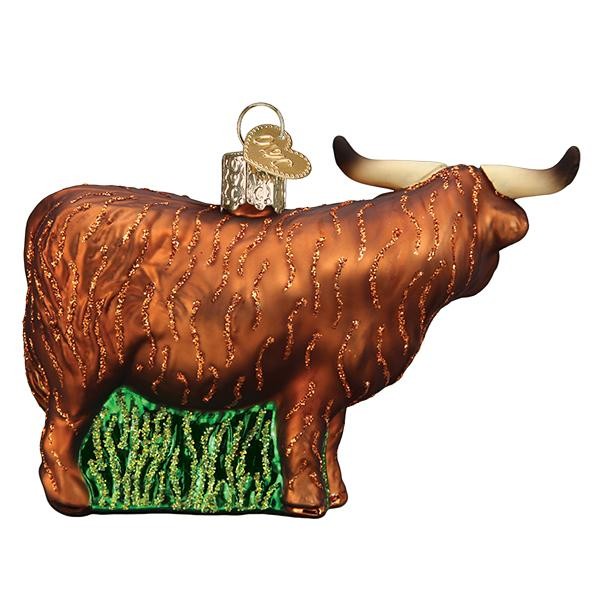 Mellow Monkey Highland Cow blown glass ornament with long horns and shaggy brown coat, on green grass base.