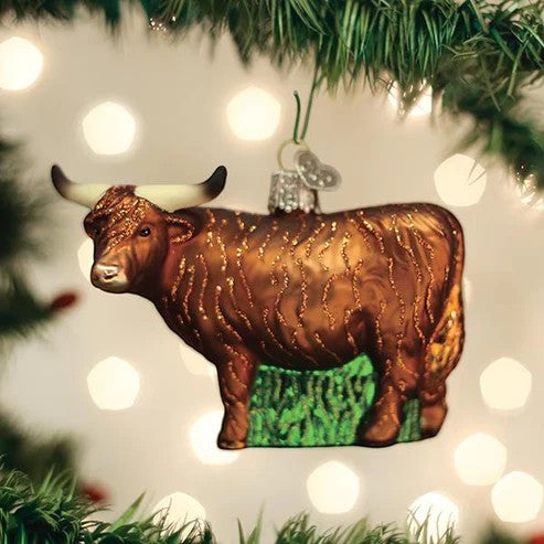 Mellow Monkey Highland Cow blown glass holiday ornament with glittery brown coat and long horns, on a Christmas tree.