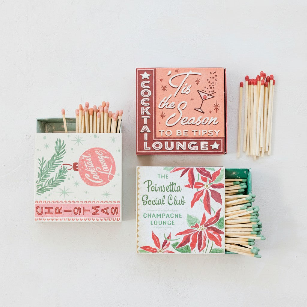 Mellow Monkey holiday matchboxes with retro graphics and coordinating colored matchsticks on a white background