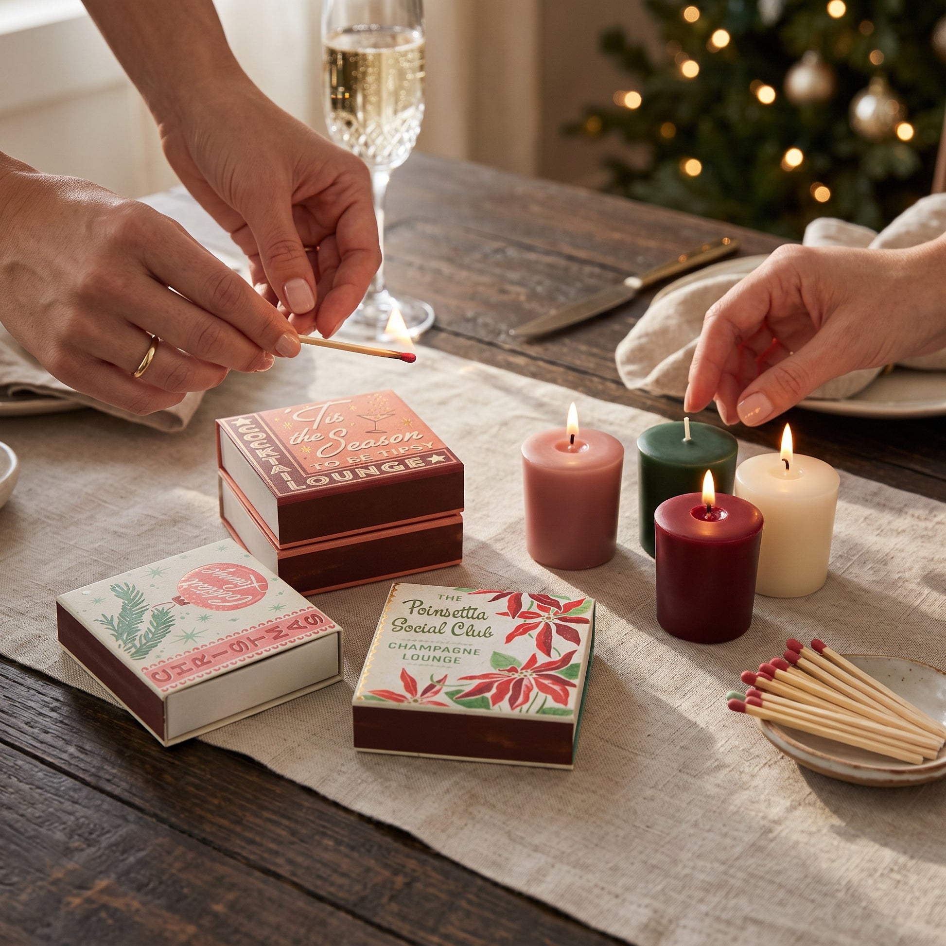 Mellow Monkey holiday matchboxes with festive graphics and colored matches on a table with candles and champagne