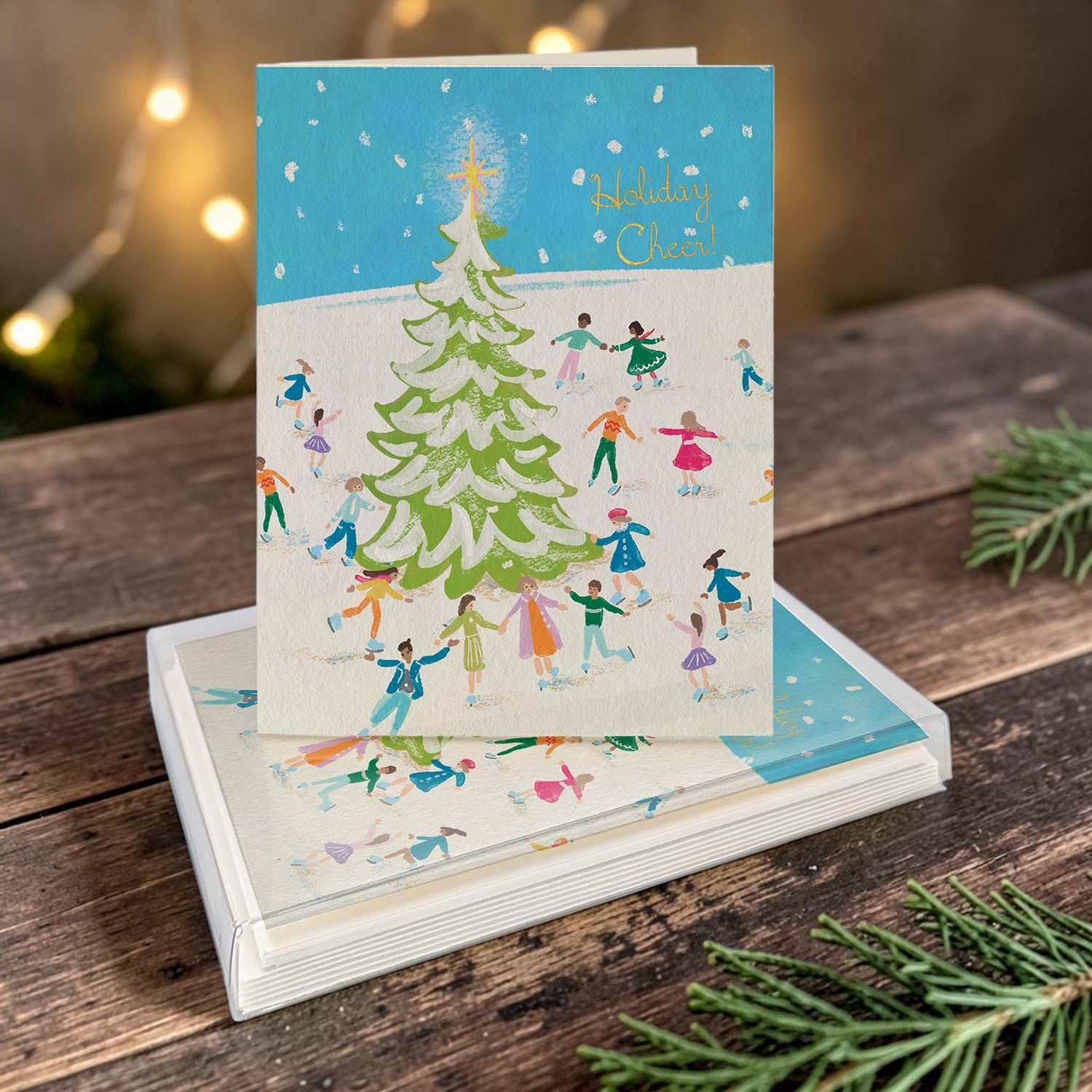 Mellow Monkey boxed holiday cards featuring a festive illustration of people ice skating around a decorated tree.