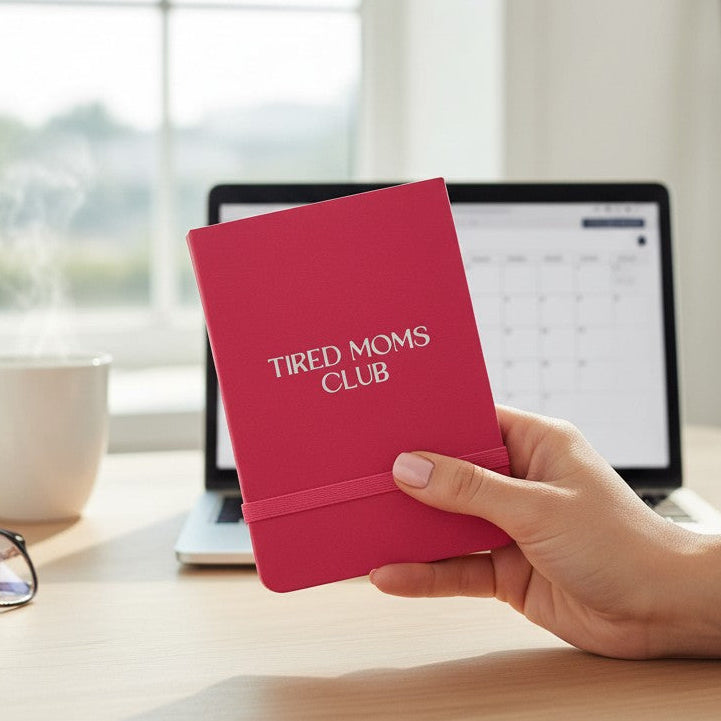 Mellow Monkey hot pink Tired Moms Club pocket notebook held in hand on a desk with a laptop and coffee.