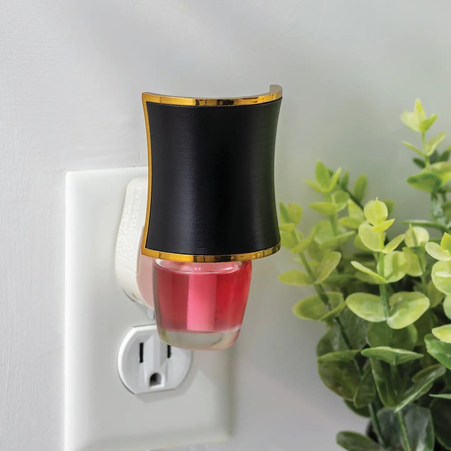 Mellow Monkey Hourglass WallScents fragrance warmer in black and gold with a pink oil refill plugged into a wall outlet