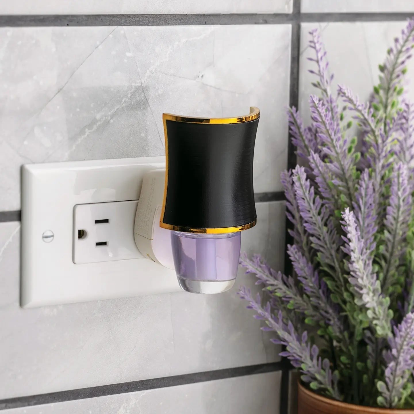 Mellow Monkey Hourglass WallScents fragrance warmer in black with gold trim plugged into a wall outlet.