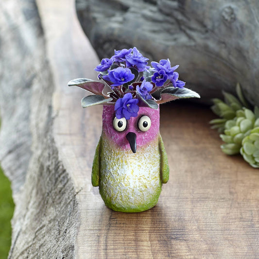 Mellow Monkey Flit Hummingbird Blobhouse Planter, a whimsical poly-resin pot with pink face, green body, and large googly eyes, holding purple flowers.