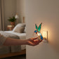 Mellow Monkey hummingbird stained glass nightlight with teal and blue glass, copper finish, plugged into a wall outlet